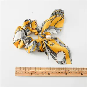 Detail view of yellow silk scrunchie with chain patterns, pearl charm, and long bow ribbons