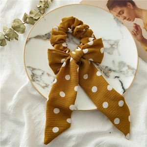 Detail view of ginger yellow polka dot bow scrunchie on a decorative marble tray
