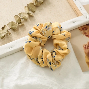 Detailed close-up of yellow floral chiffon scrunchie with blue leaves on white fabric