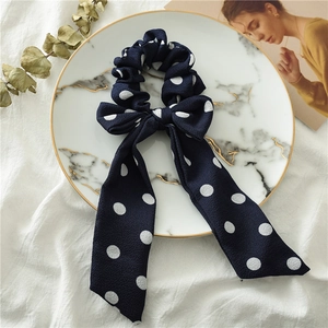 Close-up of dark blue polka dot hair scrunchie with long ribbons on marble tray