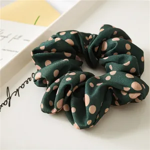 Deep green polka dot scrunchie made of soft satin fabric on a white aesthetic tray