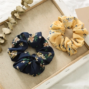 Detail view of two floral chiffon scrunchies in navy and yellow on a linen background