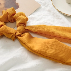 Detail of yellow textured hair scrunchie with long ribbon on a minimal background