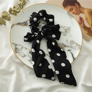 Close-up of black and white polka dot bow scrunchie with long ribbons on marble tray
