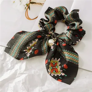 Detail view of black vintage bow scrunchie with floral pattern and pearl pendant charm