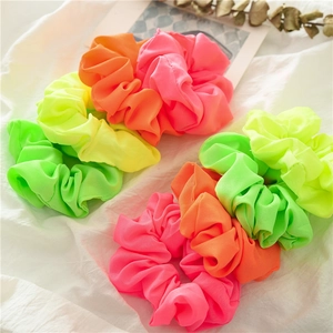 Dettaglio di elastici scrunchie neon in rosa, arancione e giallo su tessuto bianco