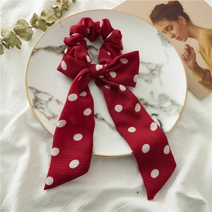 Detail of red polka dot chiffon hair scrunchie with long bow ribbon on marble plate