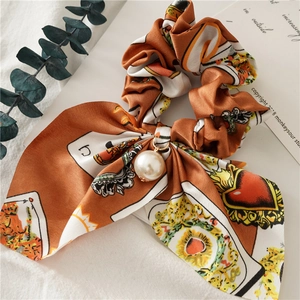 Close-up of orange silk scrunchie with poker patterns, pearl charm and bunny ear bow