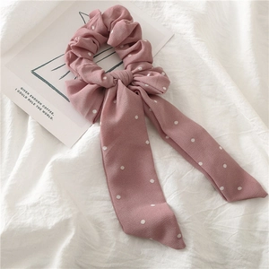 Détail d'un chouchou en mousseline rose à pois avec un long ruban en forme de nœud