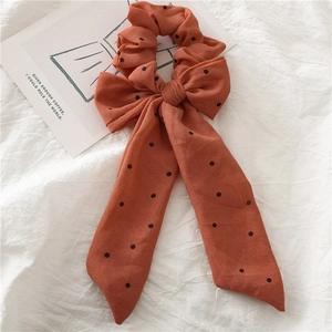 Gros plan du chouchou en mousseline orange à pois avec un long ruban sur tissu blanc