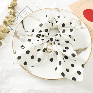Détail d'un chouchou en mousseline blanche à pois noirs avec un pendentif en perle élégant