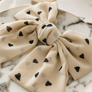 Detailed close-up of cream chiffon bow hair clip with black heart print on marble plate