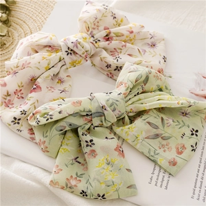 Detail of oversized floral chiffon bow hair clips in light beige and green floral patterns