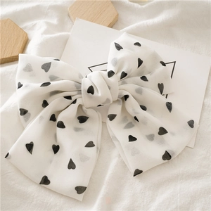 Detail of a large cream chiffon bow hair clip with black heart patterns on a soft background