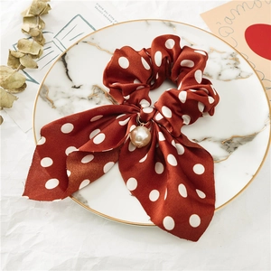 Détail de chouchou en satin rouge à pois avec perle élégante et pendentif doré
