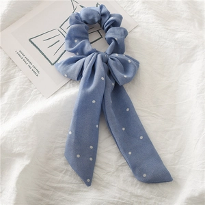 Détail d'un chouchou en mousseline à pois bleu clair avec rubans sur lin blanc