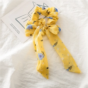 Chouchou en mousseline fleurie jaune avec long ruban sur tissu blanc plissé