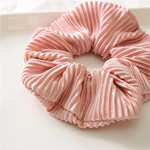 Close-up of pink satin scrunchie with pleated texture on a white decorative tray