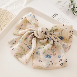 Detail of oversized floral chiffon bow hair clip on a white plate with elegant scene