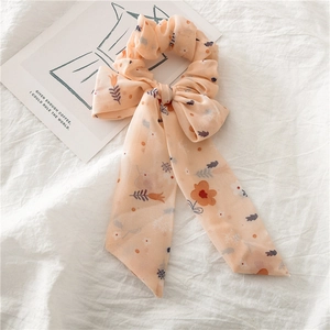 Détail d'un chouchou en mousseline orange clair à fleurs avec ruban et nœud papillon