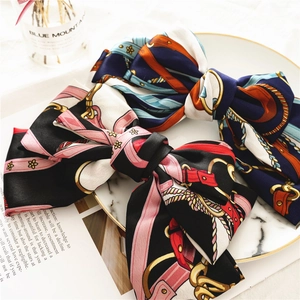 Detailed view of layered satin bow hair clips with luxury chain patterns on marble tray