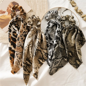 Detail of leopard and snake print hair scrunchies with long ribbons on marble surface