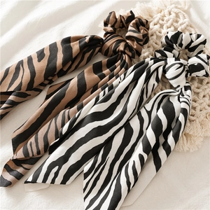 Detail view of two animal print silk scrunchies with long ribbons on a textured background