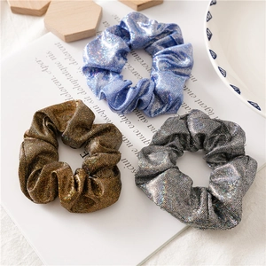 Detailopname van metallic kunstlederen scrunchies in sprankelend blauw, goud en zilver