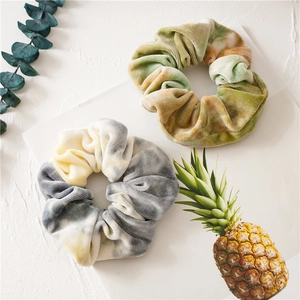 Tie-dye velvet scrunchies in yellow and green tones on a textured white surface