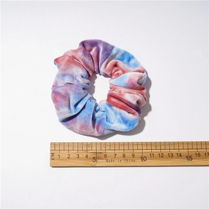 Size demonstration of tie-dye velvet hair scrunchie showing 10cm diameter on a wooden ruler