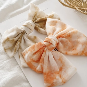 Détail du nœud papillon en tissu tie-dye rose orangé et marron olive avec barrette