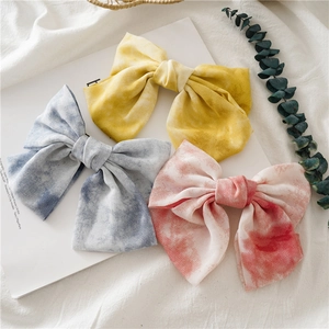 Gros plan de trois pinces à cheveux nśud tie-dye en tissu jaune, bleu et rose