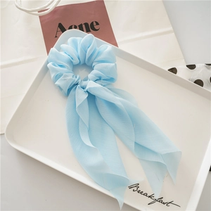 Detail of light blue chiffon scrunchie with long ribbons on a white minimalist tray
