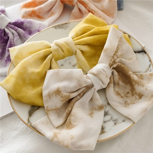 Gros plan de quatre pinces à cheveux nuds en tissu tie-dye sur un plateau en marbre