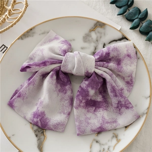 Vue détaillée d'une barrette nœud tie-dye violette sur un plat en marbre et eucalyptus