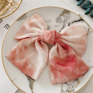 Détail d'une pince à cheveux nœud papillon tie-dye rose sur plateau marbre
