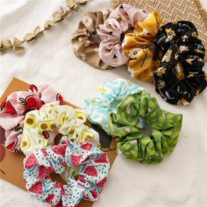 Flat lay of diverse floral and fruit pattern scrunchies on a soft white fabric background