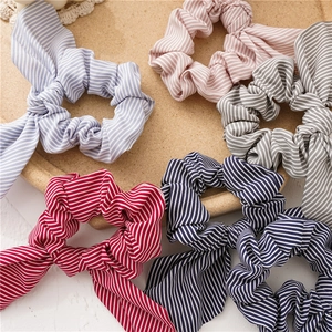 Detail showing five colors of striped rabbit ear scrunchies on a cork tray with lace background