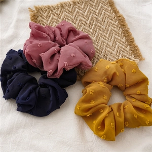Detailed texture of three velvet polka dot scrunchies in blue, pink, and yellow fabric