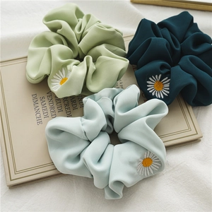 Dettaglio di tre elastici scrunchie in raso verde con ricamo margherita su libro