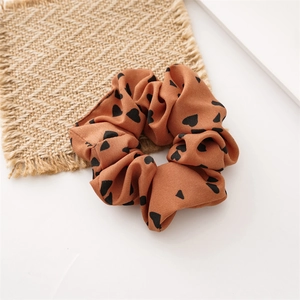 Dettaglio dell'elastico scrunchie color caramello con cuori neri su sottopentola in iuta
