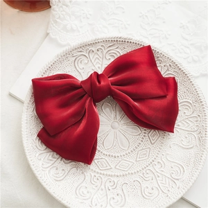 Détail d'une pince à cheveux à double nœud en satin rouge sur une assiette blanche