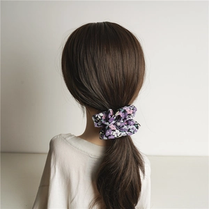 Elastico scrunchie oversize a fiori viola indossato su una coda di cavallo alta