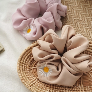 Dettaglio di elastici scrunchies rosa e kaki con ricamo margherita su cesto