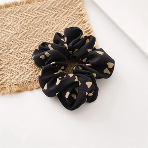 Dettaglio dello scrunchie in tessuto nero con cuori su sfondo di tappetino intrecciato