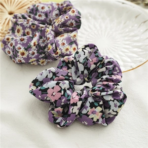 Dettaglio di due elastici floreali viola su lino bianco con elementi decorativi