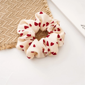 Dettaglio scrunchie crema con motivi a cuori rossi su sfondo di lino materico