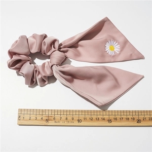 Détail d'un chouchou en satin rose avec broderie marguerite blanche et ruban noué élégant