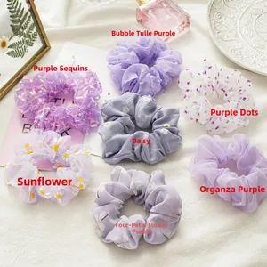 Detailset aus sieben lila Haargummis mit Blumenmustern und transparenten Texturen auf Leinen