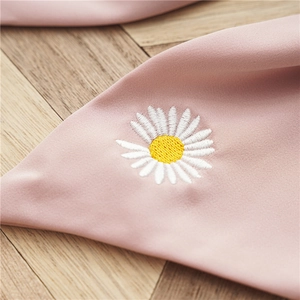 Vue détaillée de la broderie de marguerites blanches sur un tissu en satin rose